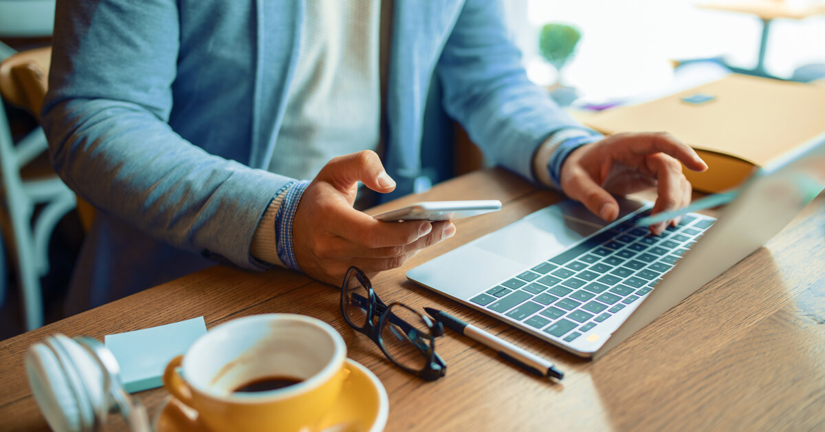 man-sitting-at-cafe-holds-phone-and-rests-hand-on-laptop