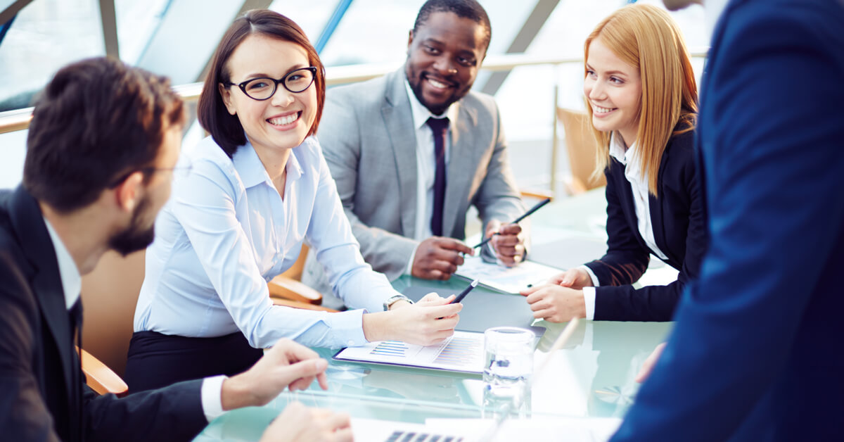 three-coworkers-smile-at-fourth-coworker-around-a-table