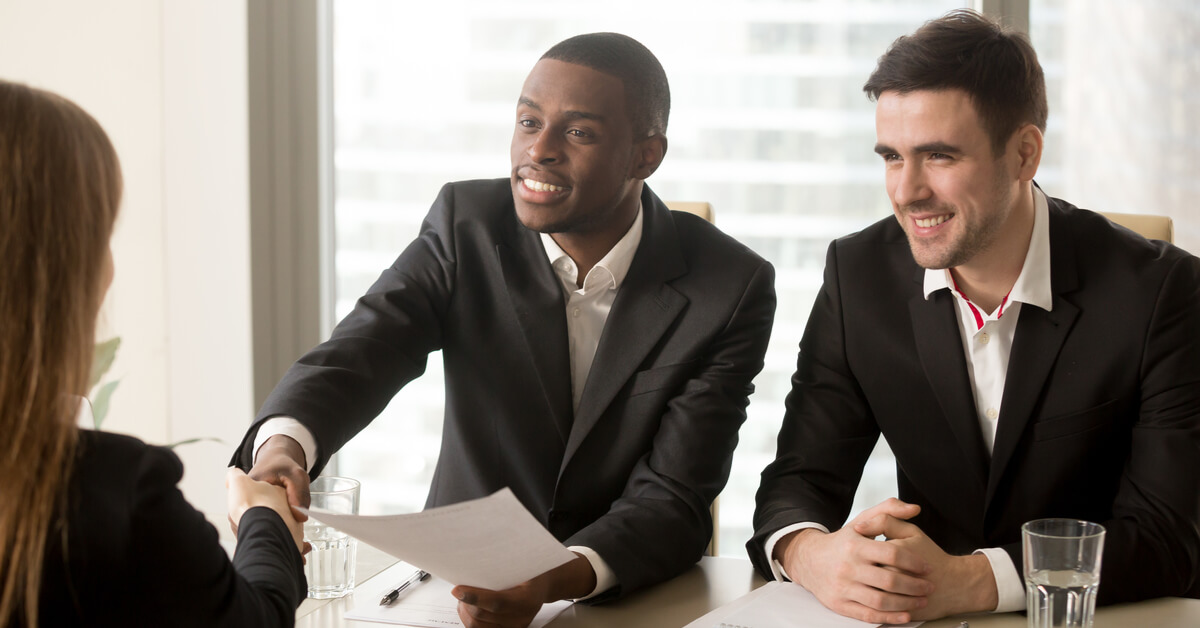 two-interviewers-sitting-at-table-one-shaking-hand-with-candidate